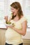 Pregnant woman in kitchen eating a salad smiling