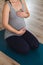Pregnant woman kneeling on yoga mat with hands on heart and belly doing prenatal yoga