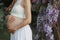 A pregnant woman in late term pregnancy in the garden of Wisteria in bloom hugs the belly