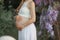 A pregnant woman in late term pregnancy in the garden of Wisteria in bloom hugs the belly