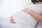 Pregnant woman leaning on the bed, close up on stomach