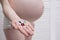 Pregnant woman in lingerie holding multicolored pills on palm on light background