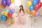 Pregnant woman with long blond hair in elegant dress, with a lot of colorful air balloons