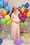 Pregnant woman with long blond hair in elegant dress, with a lot of colorful air balloons