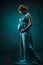 Pregnant woman in long silk dress over blue art background.