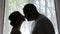 Pregnant woman and a man stand against a window in silhouette