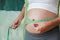 Pregnant woman measuring her belly with tape measure