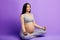 Pregnant woman mediating and keeping eyes closed while sitting in lotus position