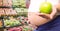 Pregnant woman mid section holding apple in blurry vegetable aisle