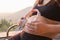 Pregnant woman putting headphones on belly on a chair at mountain sunset time