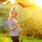 Pregnant woman on second trimester posing in sunny garden in the backlit