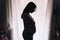 Pregnant woman silhouette standing against the window. intimate portrait expecting woman touching her big belly. concept of