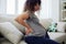 Pregnant woman sitting on the couch lower back pain and headache, strain on the spine during pregnancy. Lifestyle
