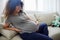 Pregnant woman sitting on the couch lower back pain and headache, strain on the spine during pregnancy. Lifestyle