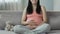 Pregnant woman sitting on couch, rubbing stomach and smiling, happy pregnancy