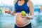 Pregnant woman in sport clothes making choice between donut and green apple