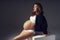 Pregnant woman in sports underwear sitting on large cube