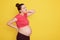 Pregnant woman standing isolated over yellow background with pain in neck and back, wearing casual red t shirt, showing her bare