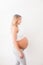 Pregnant woman is standing near white wall