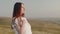 Pregnant woman stands on hill and performs breathing exercises from yoga with her hand on her chest, front view. Concept