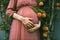 A pregnant woman stands near a tree with peach fruits. Symbol of fertility