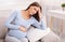 Pregnant Woman Suffering From Migraine Sitting On Couch At Home