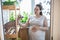 Pregnant woman talking with her bald sphynx and stroke a cat on domestic balcony in colorful flowers