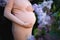 pregnant woman tenderly hugs her belly surrounded by lilac flowers