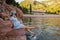 Pregnant woman traveler in denim dress, blue straw hat sits by the sea, dangles legs in water