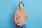 Pregnant woman with tummy-ache posing isolated over blue background, feels constructions, being very scared and worried, wearing