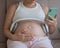 A pregnant woman turns on music for her child on a smartphone. Headphones on the tummy.