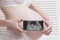 Pregnant woman in underwear holding and showing smartphone with fetal ultrasound photo on white wooden screen background. Close-up