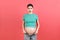 Pregnant woman in unzipped jeans showing her abdomen at colorful background with copy space