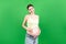 Pregnant woman in unzipped jeans using moisture cream to prevent stretch marks on her belly at colorful background with copy space