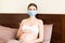 Pregnant woman is wearing protective medical mask with word. Mother is staying in bed because of respiratory disease.