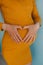 Pregnant woman in yellow dress. Pregnancy heart shape on tummy. Love sign