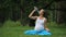 Pregnant yoga woman drinking water from a bottle, in the lotus position. park ,grass ,.outdoor, forest.