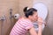 Pregnant young tired woman is vomiting in toilet sitting on the floor and drinking water.