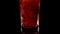 Premium Drink. Super slow motion shot of pouring pomegranate juice into a transparent glass against black background
