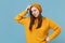 Preoccupied puzzled young brunette woman girl in yellow sweater and hat posing isolated on blue background studio