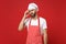 Preoccupied tired young male chef cook or baker man in striped apron toque chefs hat posing isolated on red background