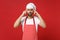 Preoccupied young bearded male chef cook or baker man in striped apron toque chefs hat posing isolated on red wall