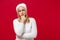 Preoccupied young woman in white sweater hat isolated on red background, studio portrait. Healthy fashion lifestyle