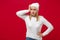 Preoccupied young woman in white sweater, hat isolated on red wall background, studio portrait. Healthy fashion