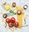 Preparation of appetizing Italian pasta, with tomatoes, basil, and oil in a decanter, spices seasonings on a white rustic back