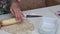 Preparation of cinnabons. A woman rolls out a ball of dough on the table. Wooden rolling pin. The camera moves on a slider. Close-