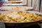 Preparation of paella in large frying pans standing in a row. Vegetables, spices and chicken meat are steamed in big pans to prepa