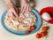 The preparation of a perfect Italian pizza with a female hand that adds all the ingredients