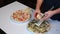 Preparation of pizza. The man rubs cheese on a grater on a pizza with crab sticks and leaves.