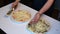 Preparation of pizza. The man rubs cheese on a grater on a pizza with crab sticks and leaves.